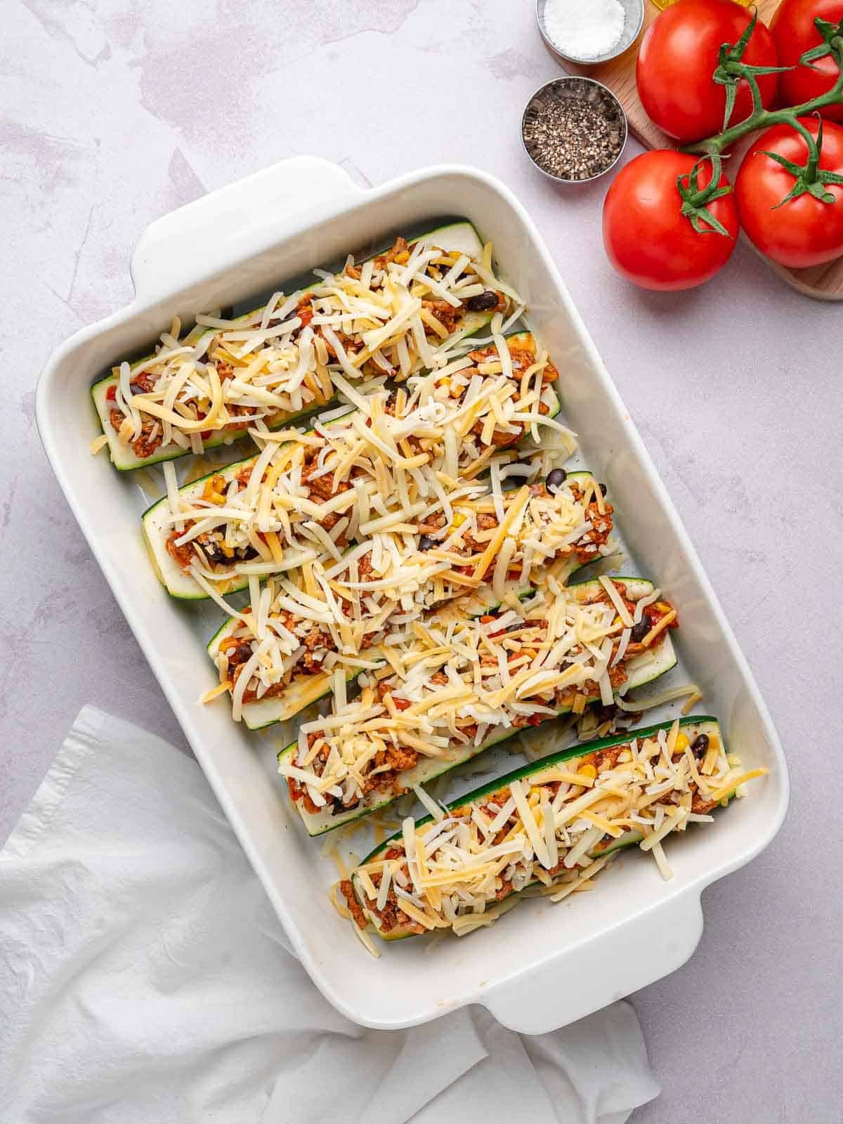 Stuffed zucchini topped with shredded Mexican cheese before baking.