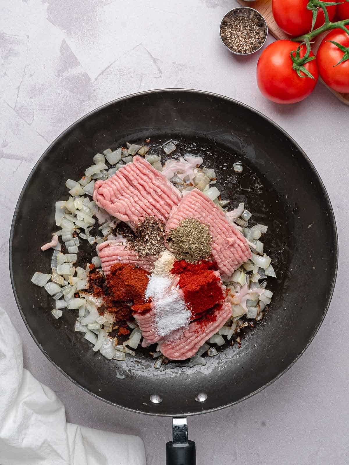 Ground turkey with sautéed onion and seasonings in a skillet.