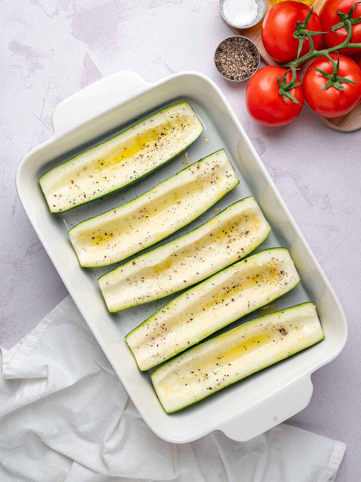 Hollowed zucchini with olive oil, salt, and pepper in a baking dish.