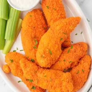 A plate of buffalo chicken fingers with celery and dip.