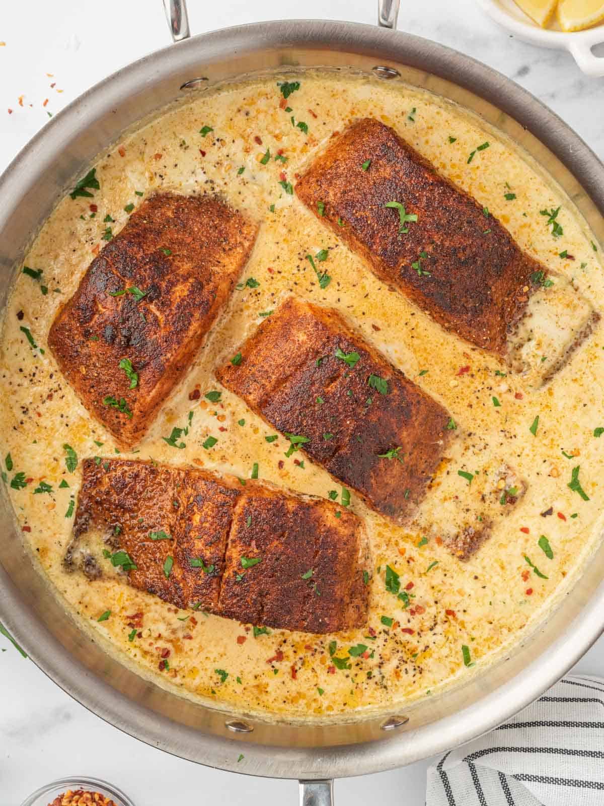 Salmon bathed in creamy sauce in a skillet.