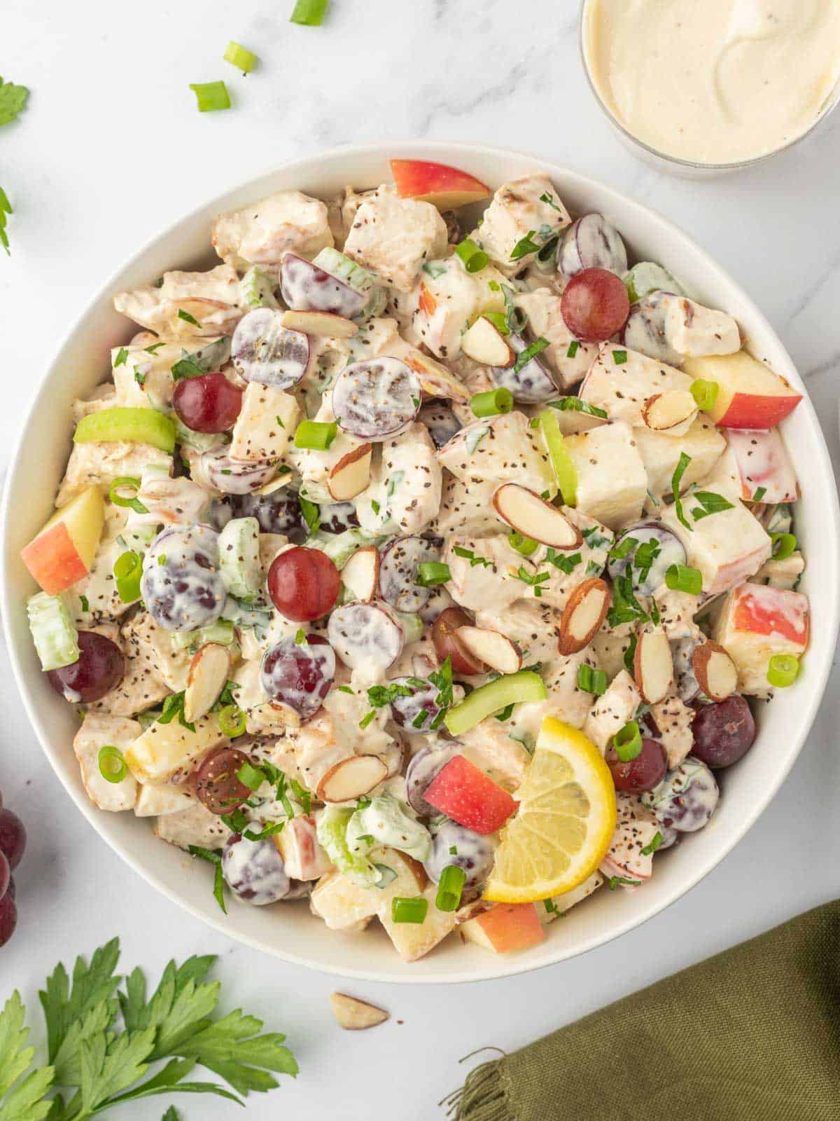 A bowl of chicken salad with grapes and apples.