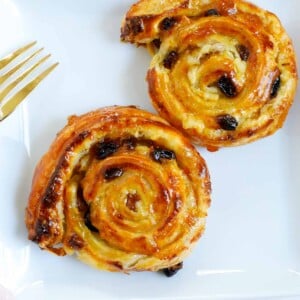 two baked pain aux raisins on a white plate.