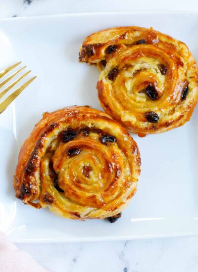 two baked pain aux raisins on a white plate.