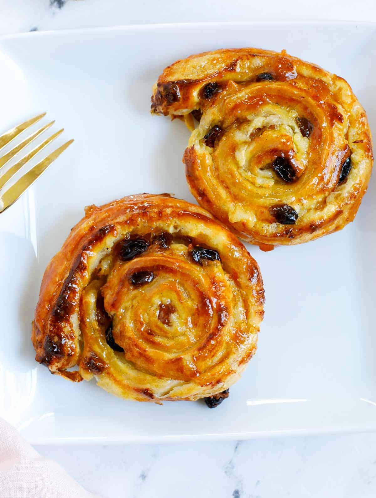 two baked pain aux raisins on a white plate.