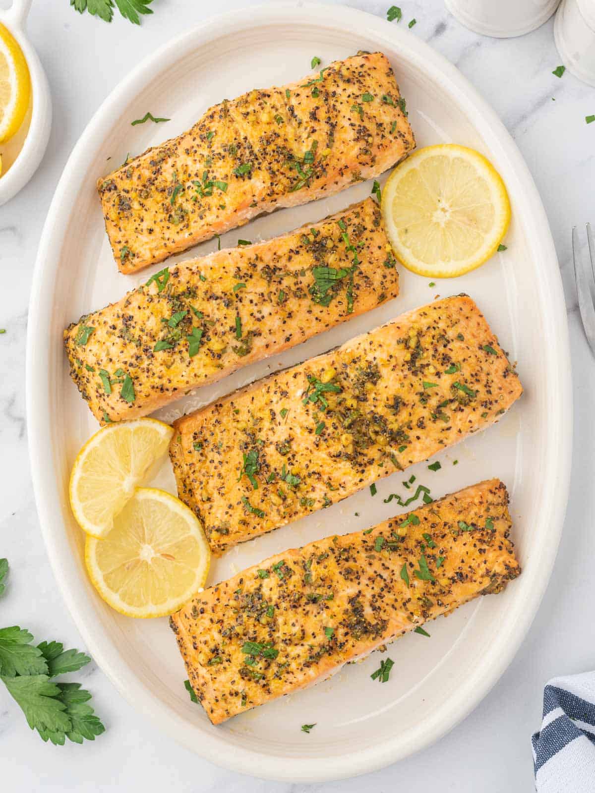 Lemon pepper baked salmon on a platter garnished with lemon slices.