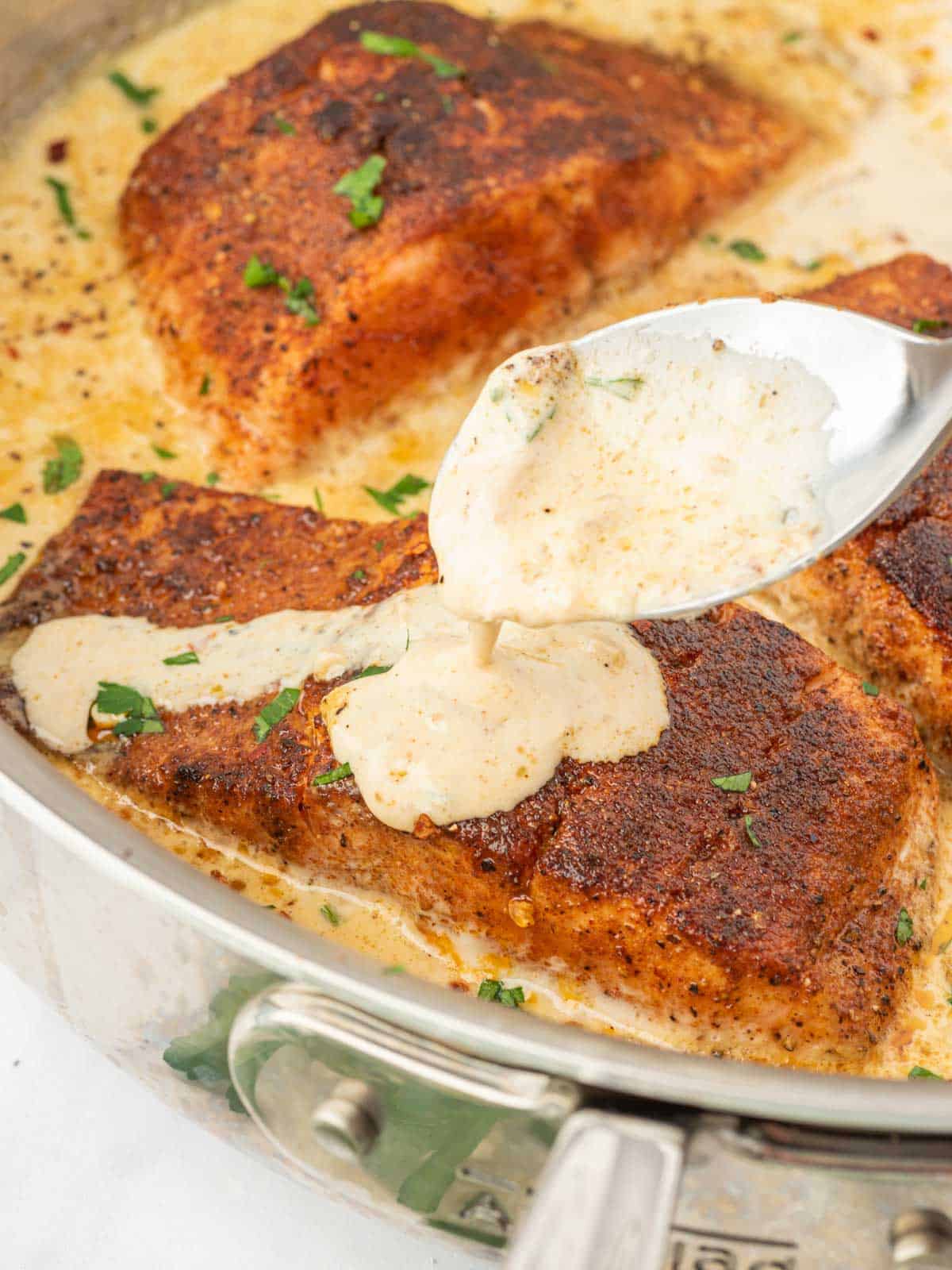 Cajun salmon with a spoon drizzling cream sauce.