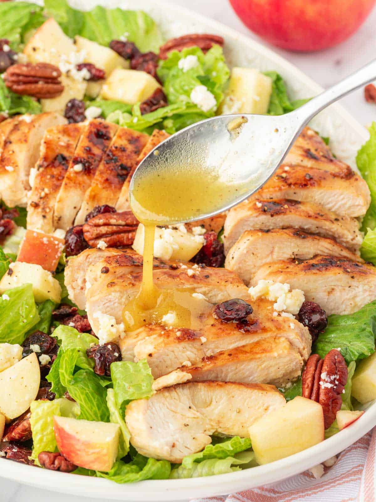 A spoon drizzles dressing over the autumn chopped salad.