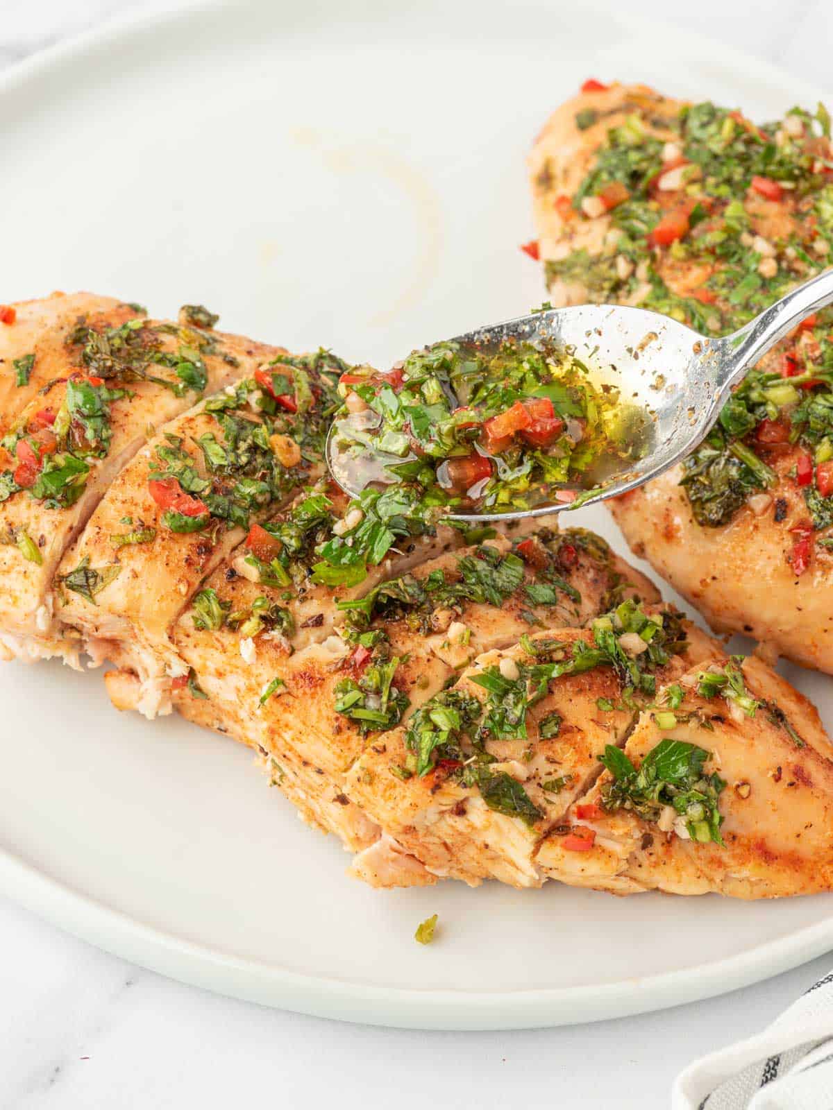 Drizzling chimichurri sauce on chicken breast.