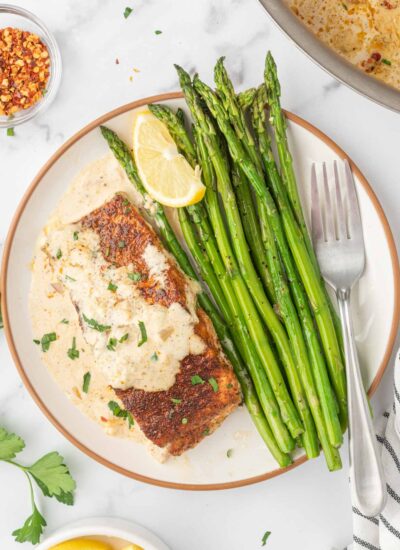 A plate with asparagus spears and a piece of salmon with cream sauce and a fork.