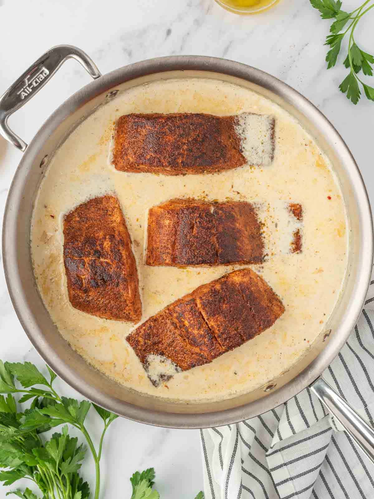 Blackened salmon in a skillet with creamy sauce.