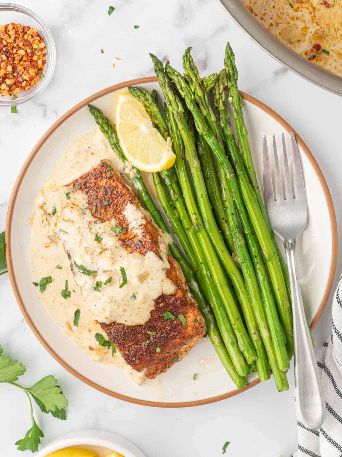 A plate with asparagus spears and a piece of salmon with cream sauce and a fork.