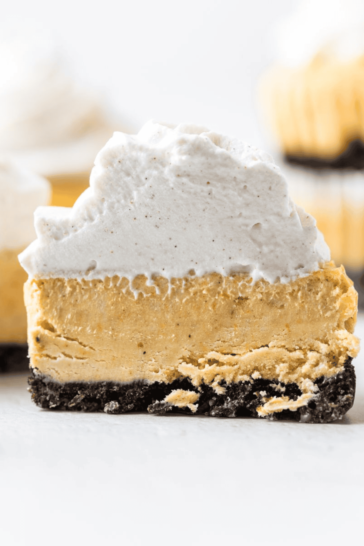 Cut pumpkin cheesecake showing the creamy filling, Oreo crust, and whipped cream topping.