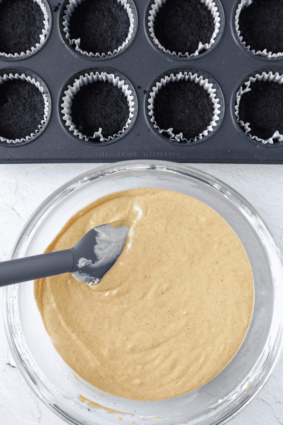 Prepared pumpkin cheesecake filling beside pre-baked Oreo crusts in cupcake liners.