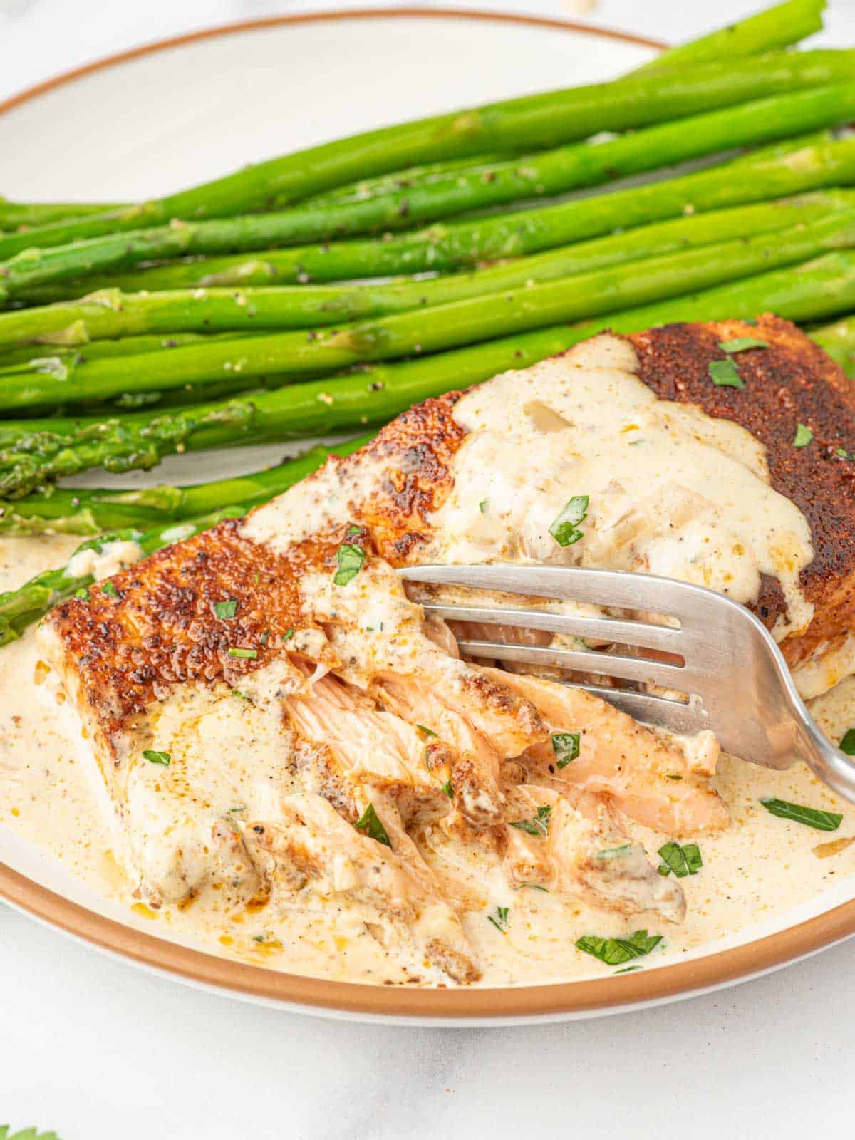 Flaking salmon with a fork on a plate with asparagus.