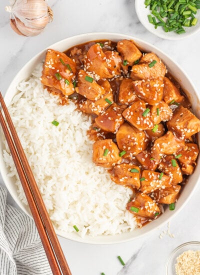 Chinese sesame chicken in a bowl with rice and chopsticks resting on the side.