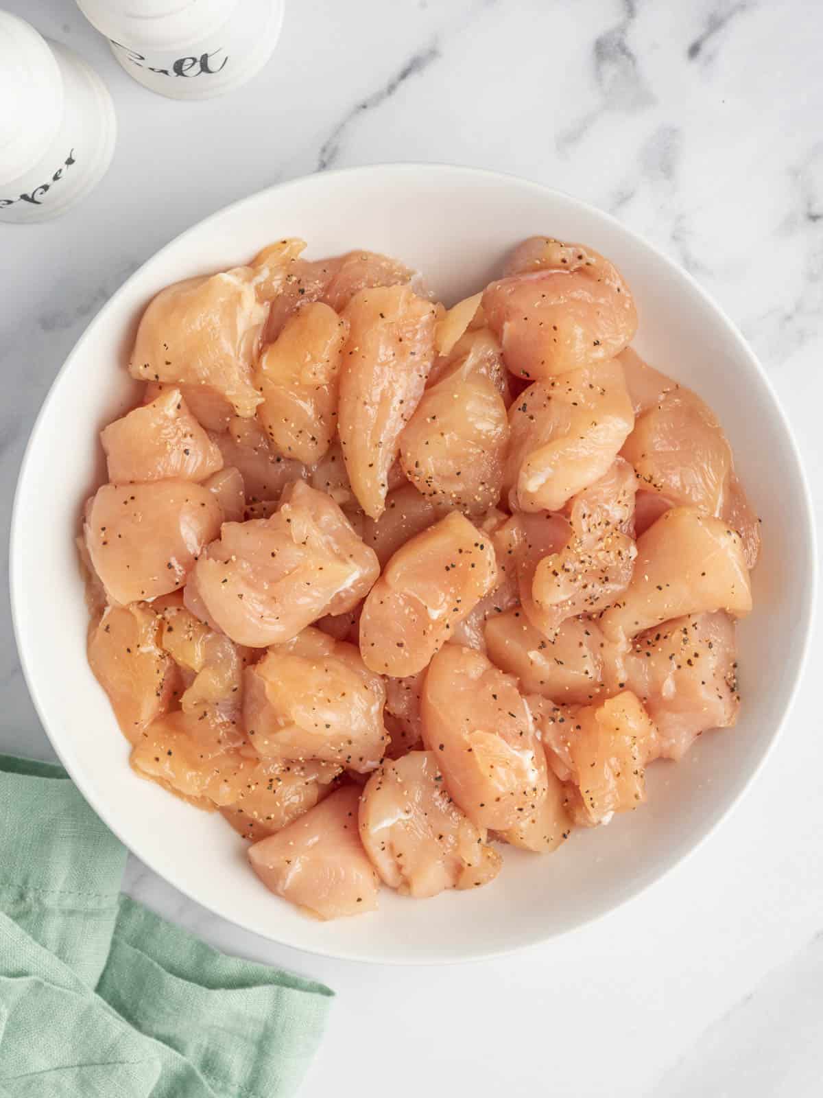 Chicken breast seasoned with salt and pepper in a white bowl.