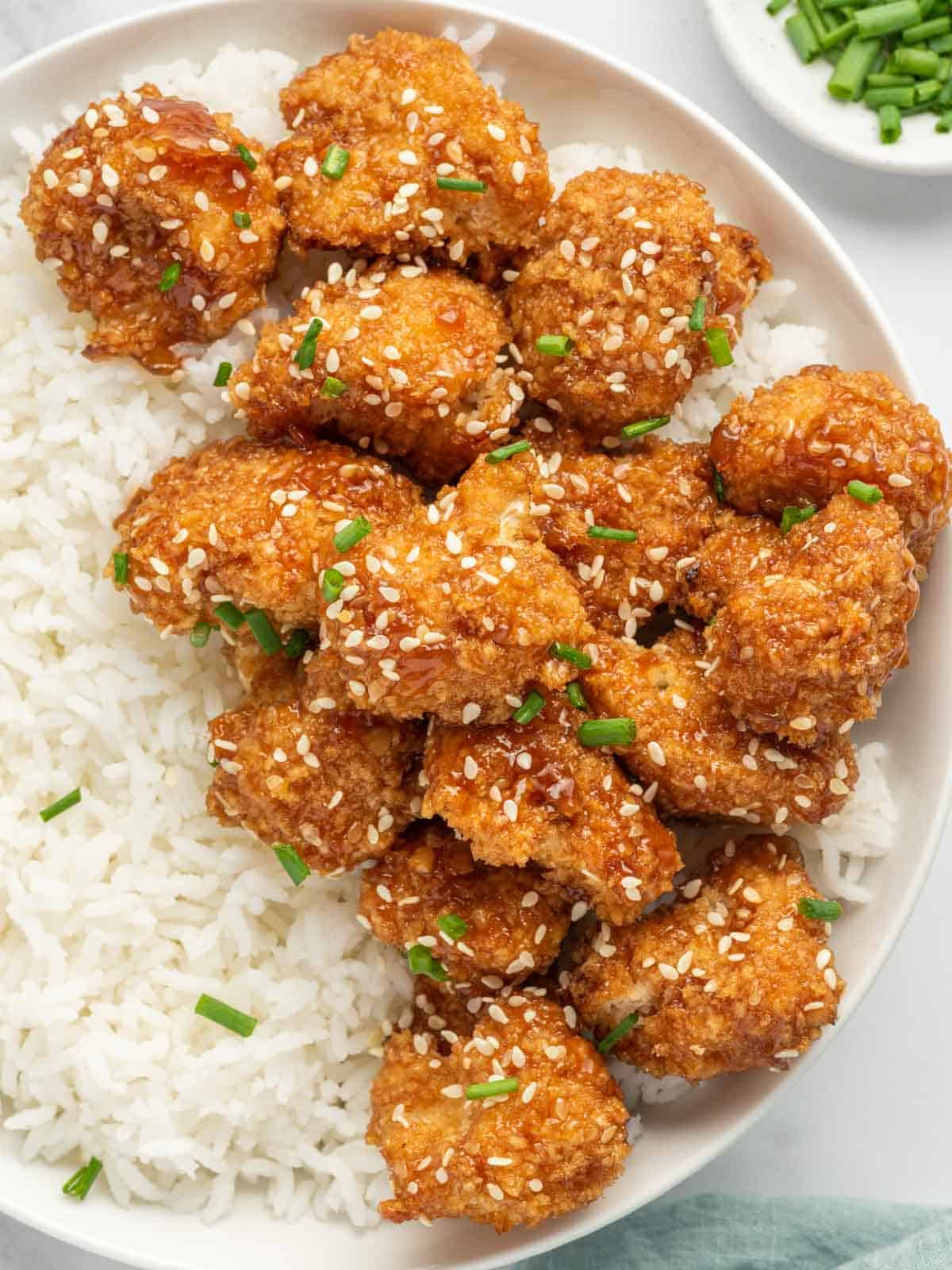 Sticky sesame cauliflower bites over rice on a white plate.