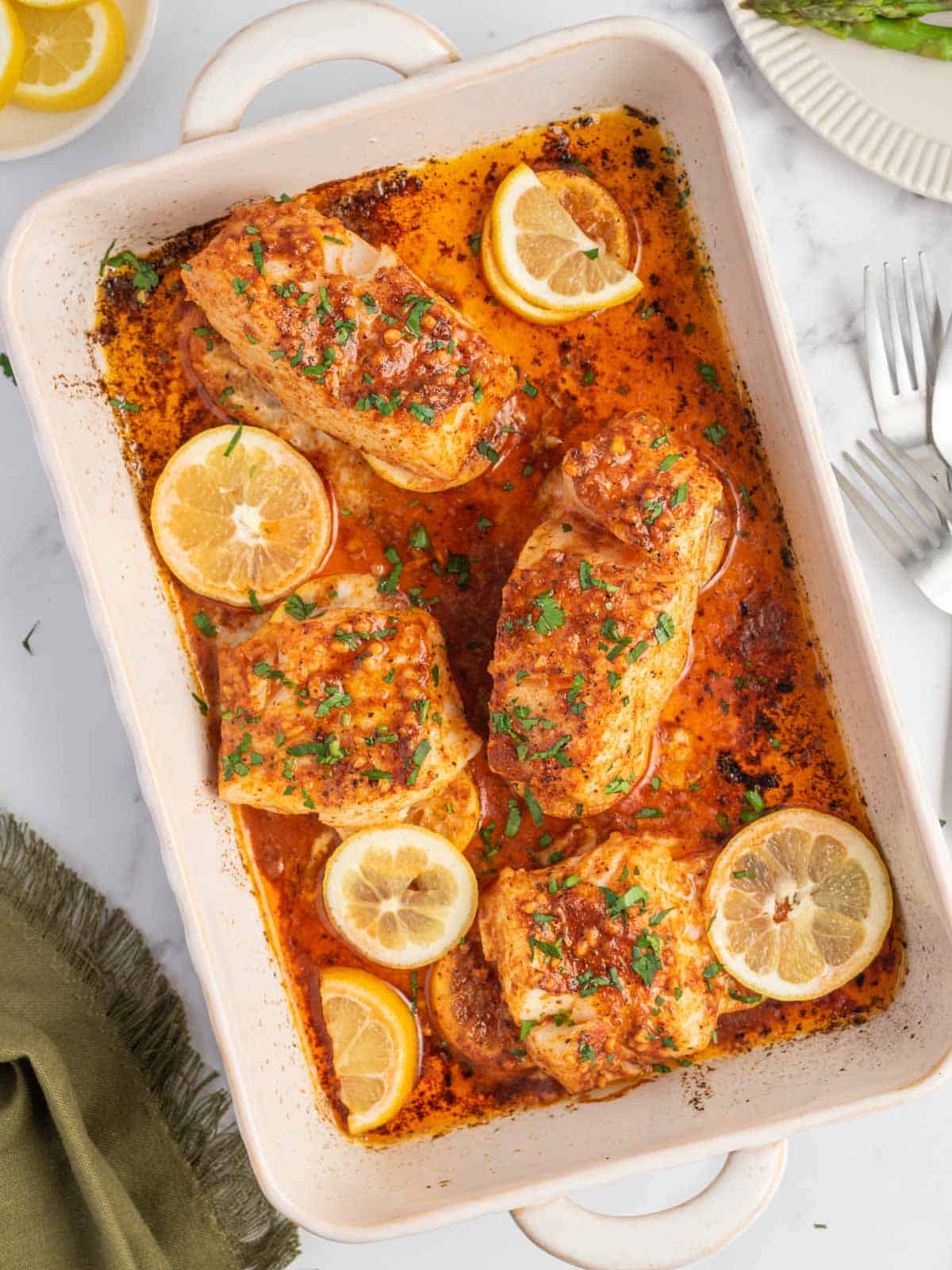A baking dish with the best baked cod topped with lemon slices.