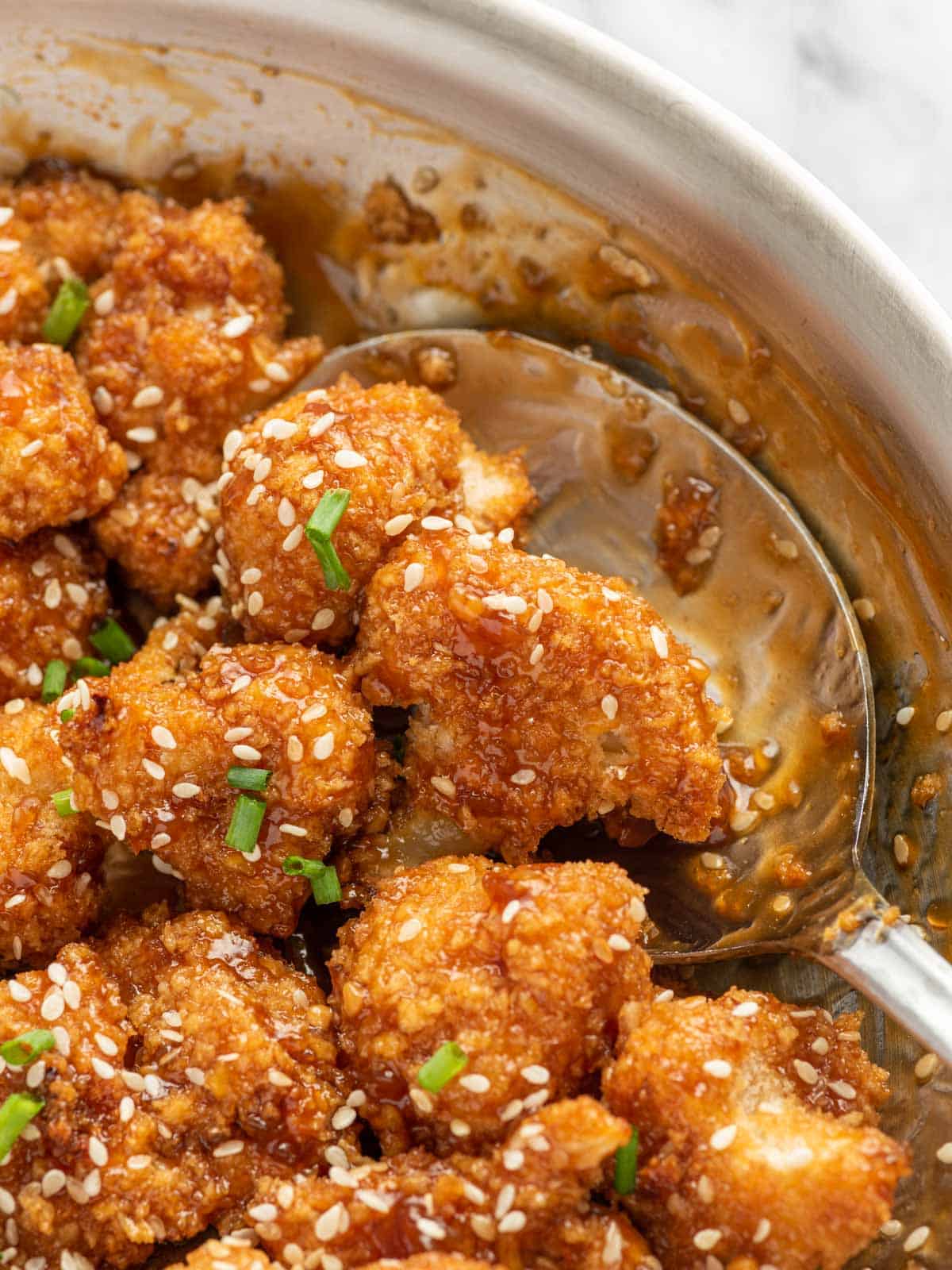 A spoon scoops a serving of asian cauliflower from a pan.