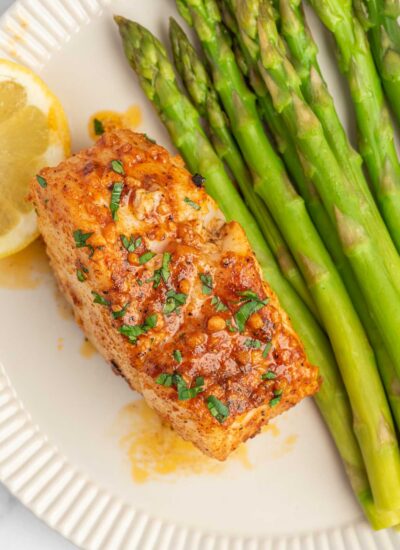 A filet of cajun cod on a plate with asparagus.