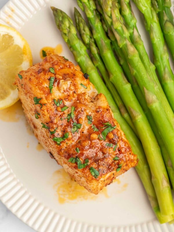 A filet of cajun cod on a plate with asparagus.