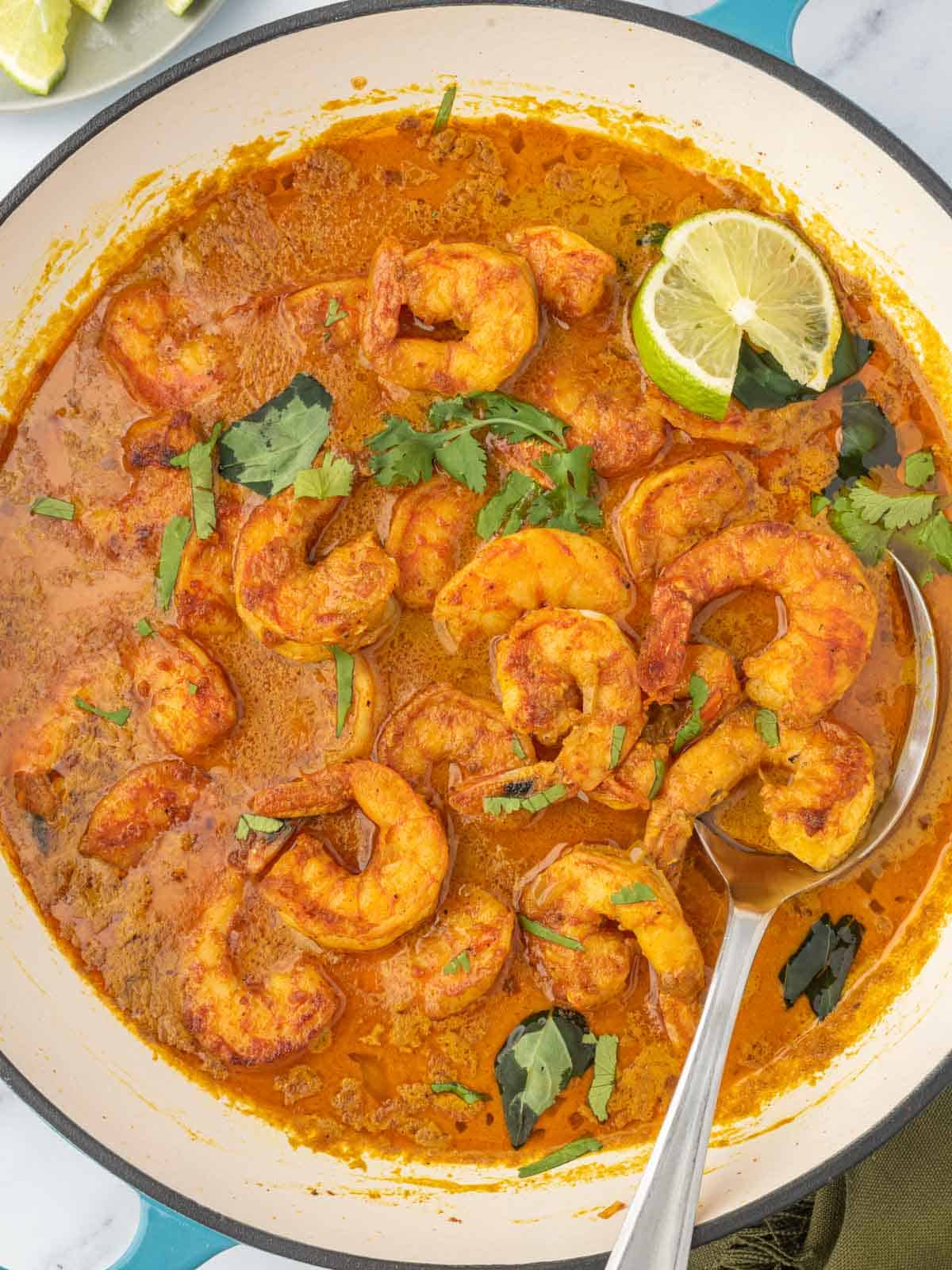A pot of red curry shrimp with a spoon.