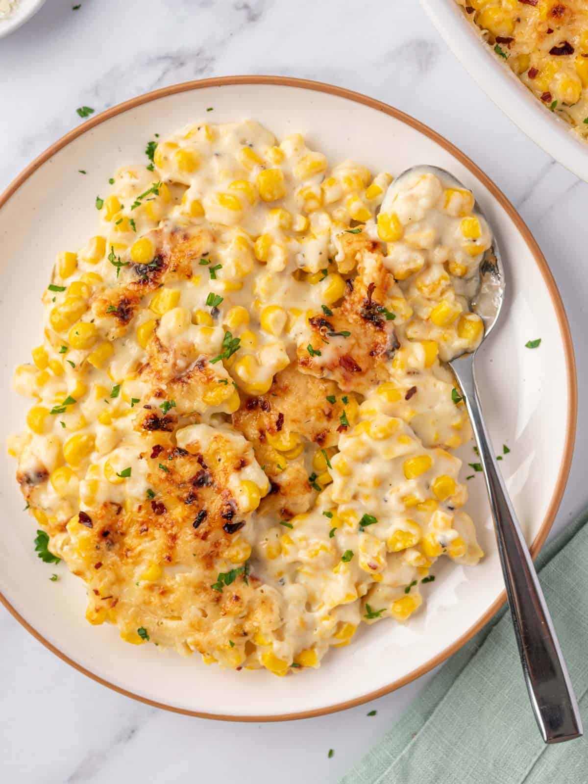 Creamy corn with browned cheese, red pepper flakes, and parsley served on a plate.