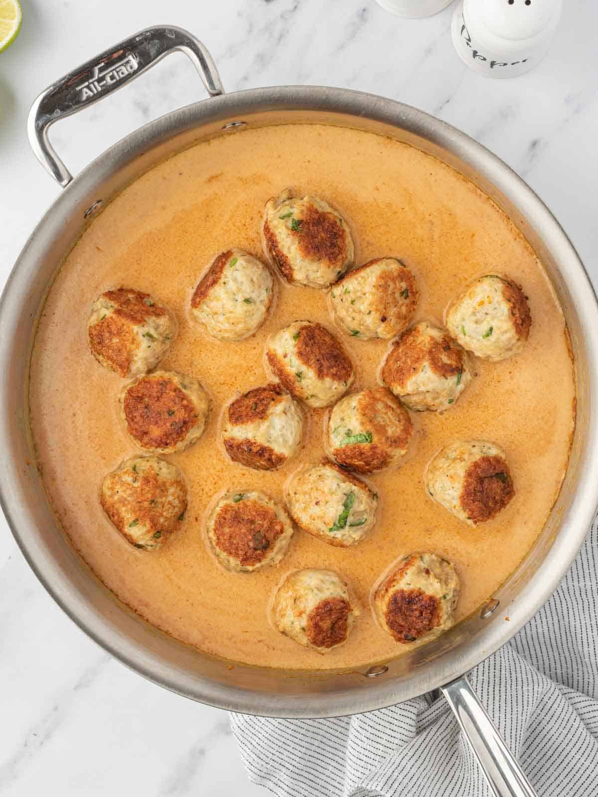 Adding meatballs to the sauce in a skillet.