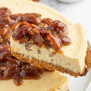 A slice of cheesecake topped with caramel pecan sauce is lifted.