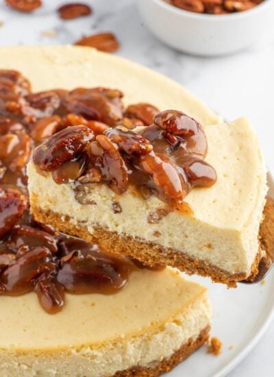 A slice of cheesecake topped with caramel pecan sauce is lifted.