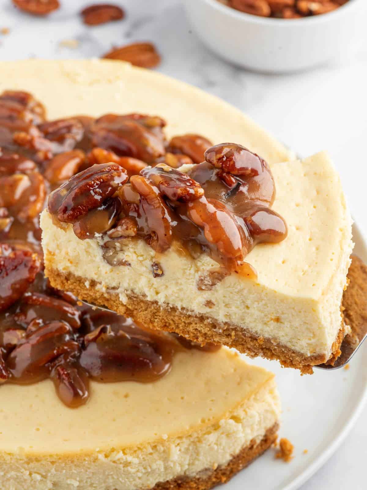 A slice of cheesecake topped with caramel pecan sauce is lifted.