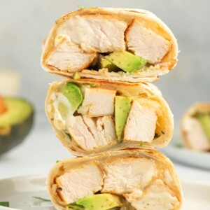 Grilled chicken, avocado and cheese in an easy chicken wrap stacked on a plate.