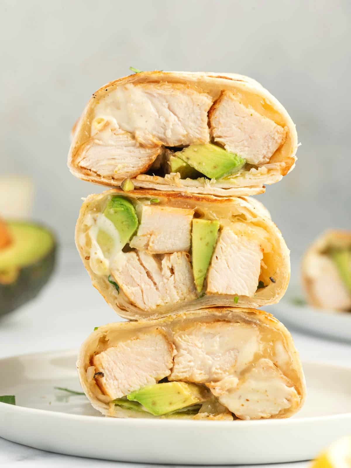 Grilled chicken, avocado and cheese in an easy chicken wrap stacked on a plate.