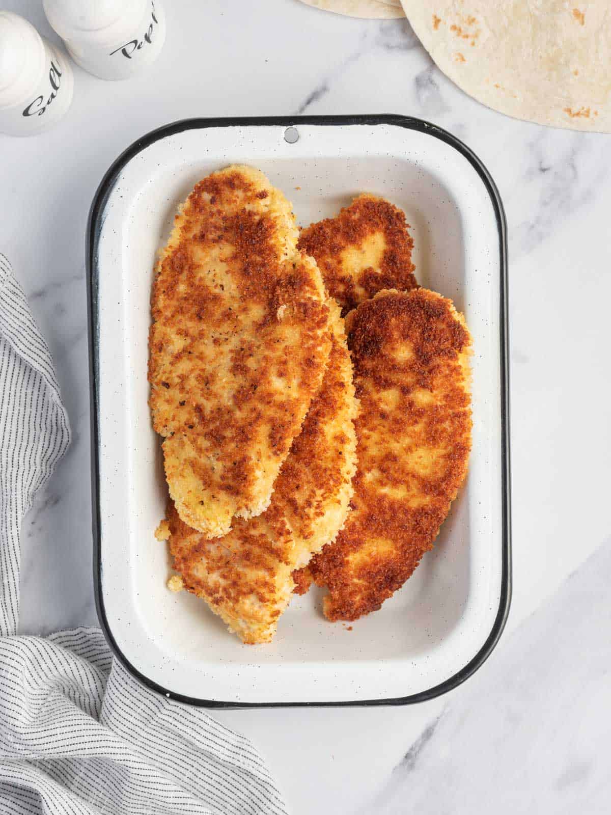 Homemade panfried chicken strips in a tray.