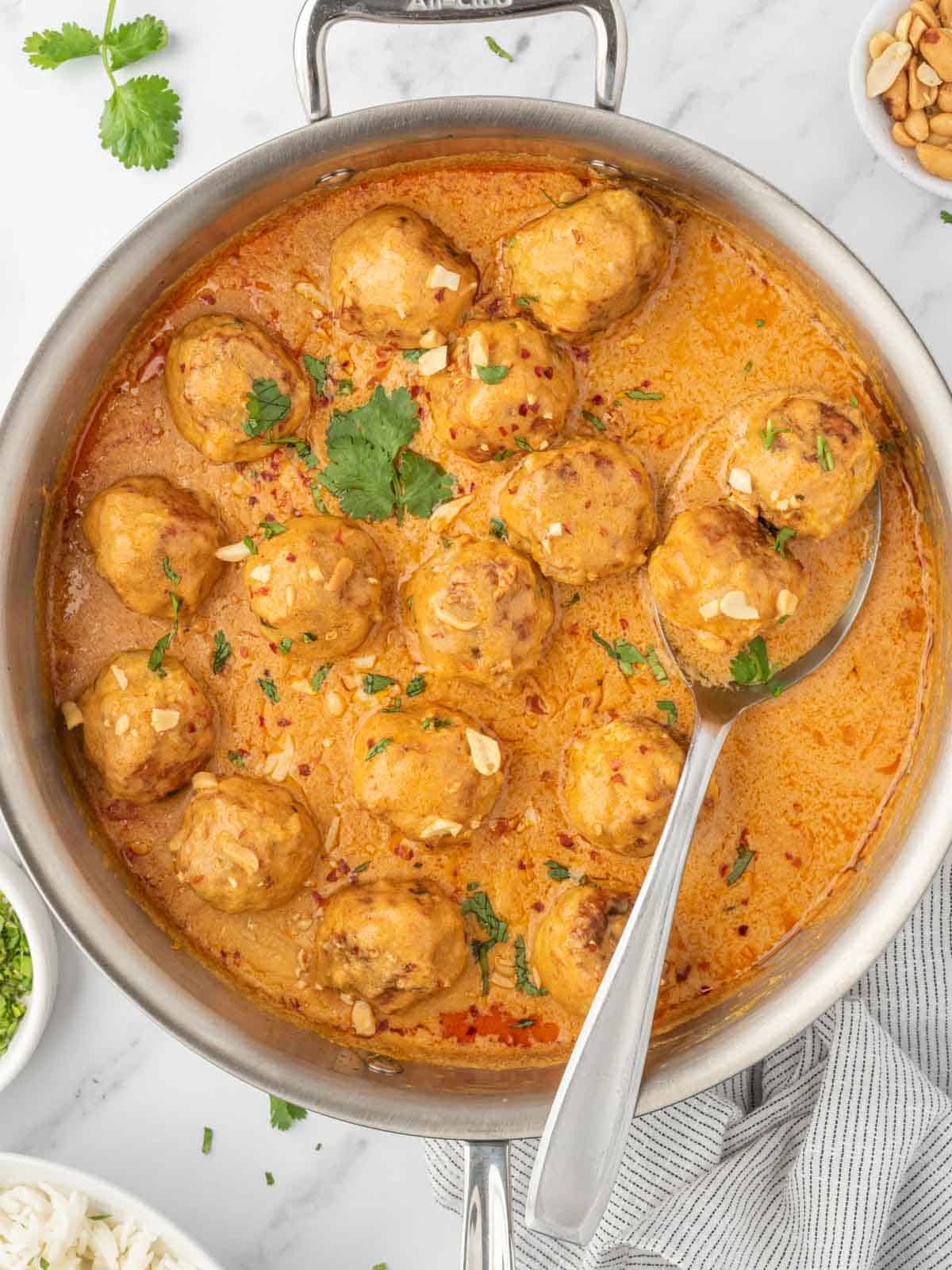 Meatballs in a skillet with coconut curry sauce.