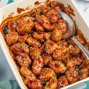 A spoon scoops baked honey sesame chicken breast from a casserole dish.