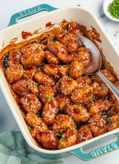 A spoon scoops baked honey sesame chicken breast from a casserole dish.