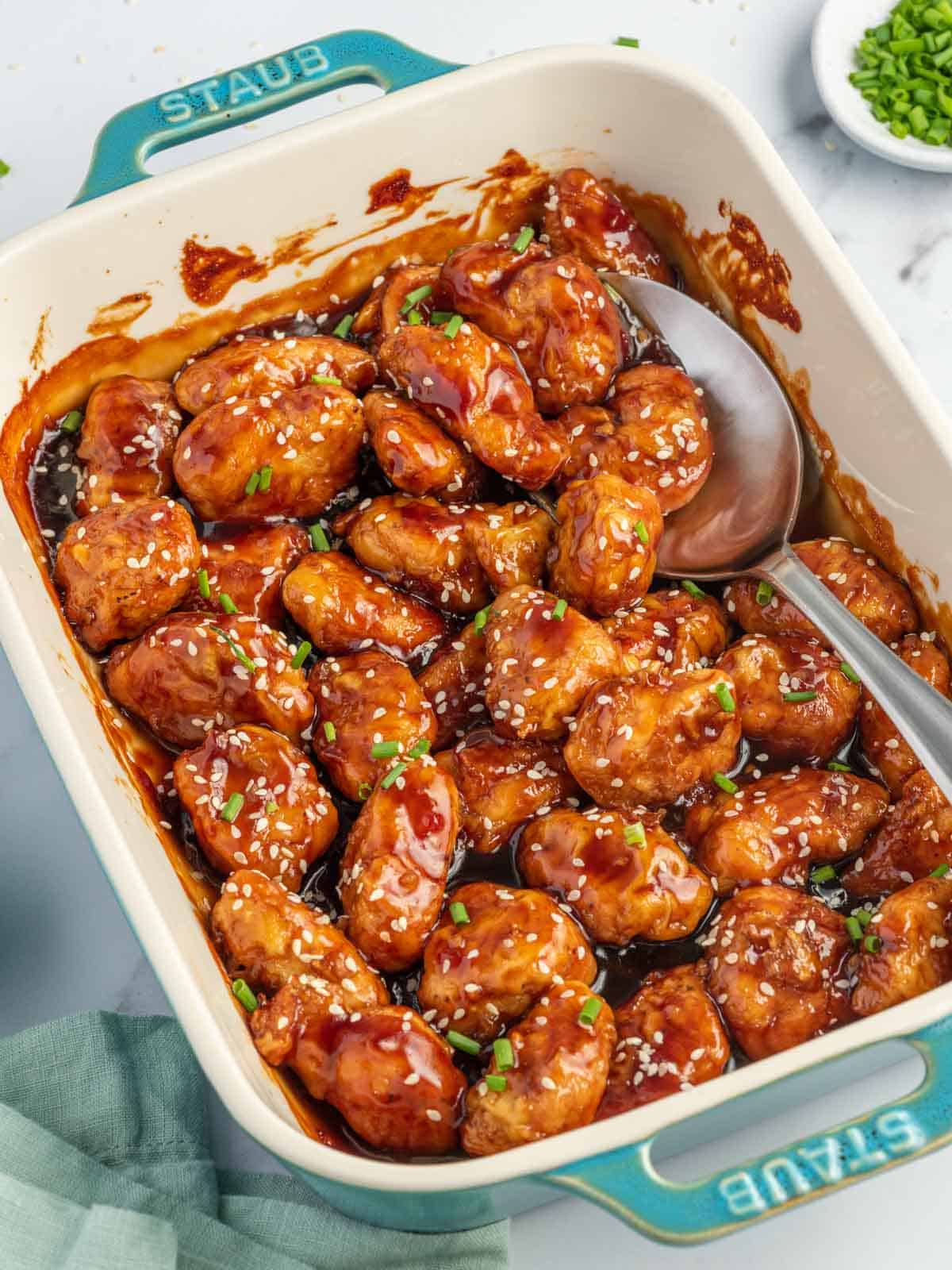 A spoon scoops baked honey sesame chicken breast from a casserole dish.