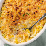 Creamy corn casserole with a golden Parmesan topping, red pepper flakes, parsley, and a spoonful served from the dish.