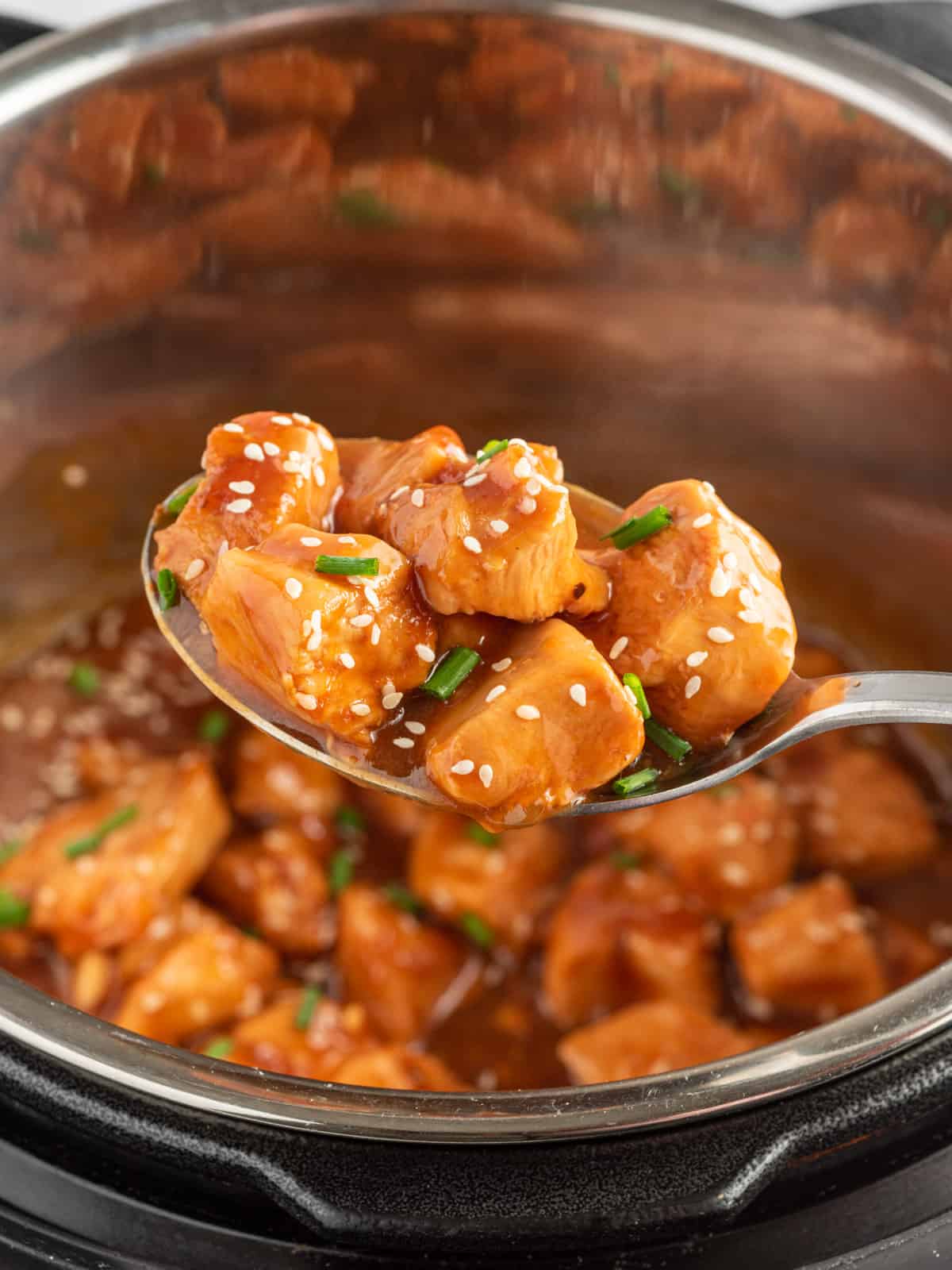 A spoon scoops chicken with sesame sauce out of pressure cooker.