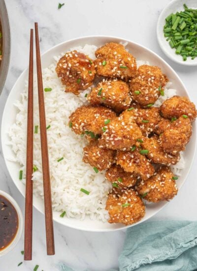 Chop sticks rest on a bowl of rice and vegan sesame cauliflower.