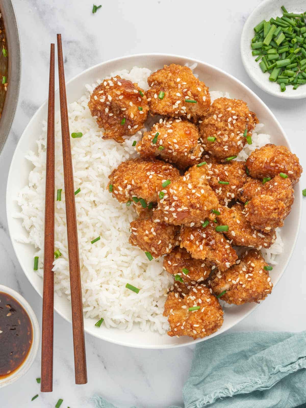 Chop sticks rest on a bowl of rice and vegan sesame cauliflower.