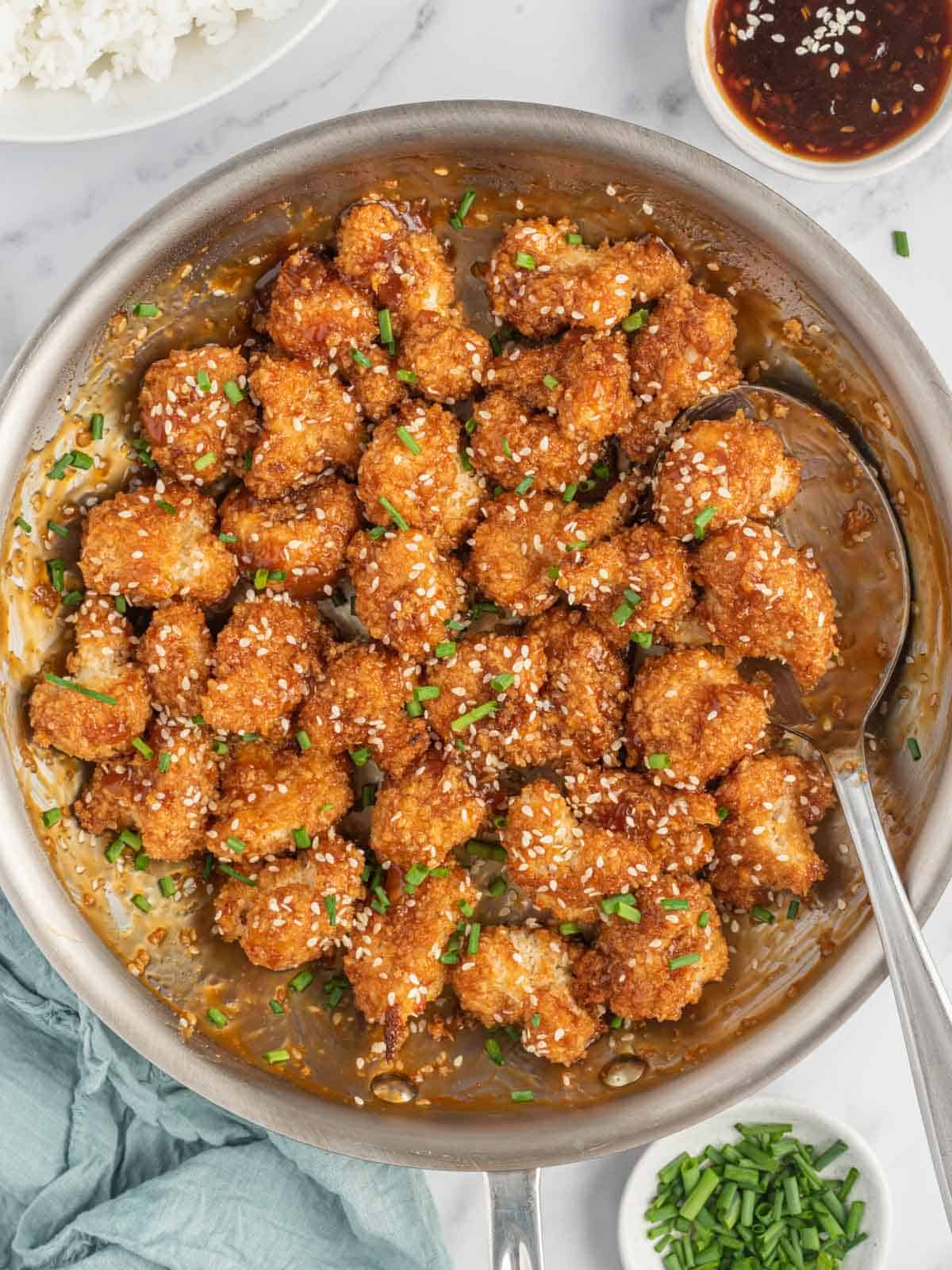 A pan of stick sesame cauliflower bites with a spoon and bowls of garnish.