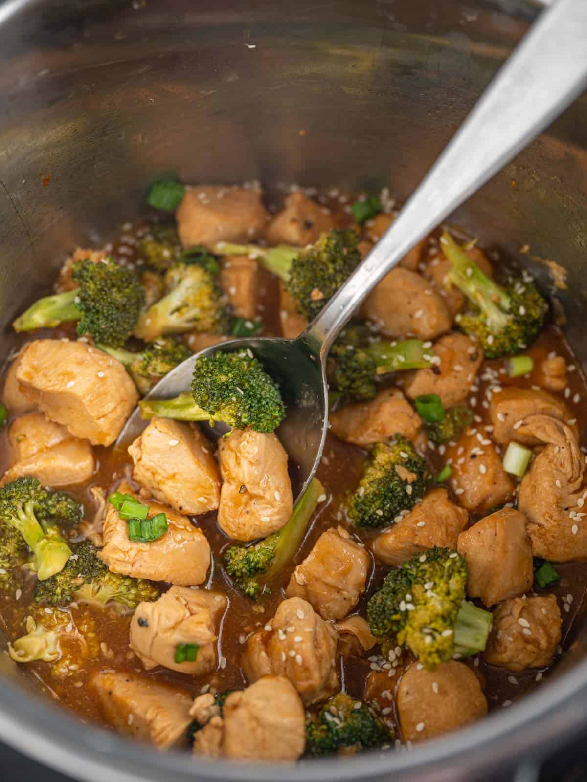 A spoon lifts a serving of chicken and broccoli from instant pot.