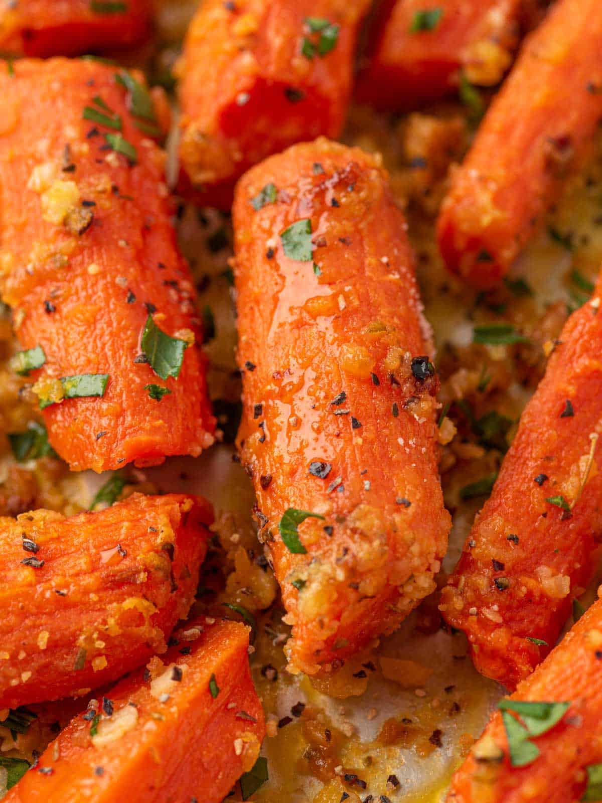 Close-up of a tender roasted carrot coated with garlic, Parmesan, and herbs.