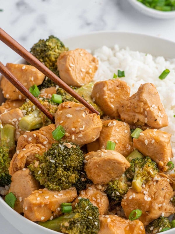 Chopsticks pick up a piece of tender chicken from a plate with rice.