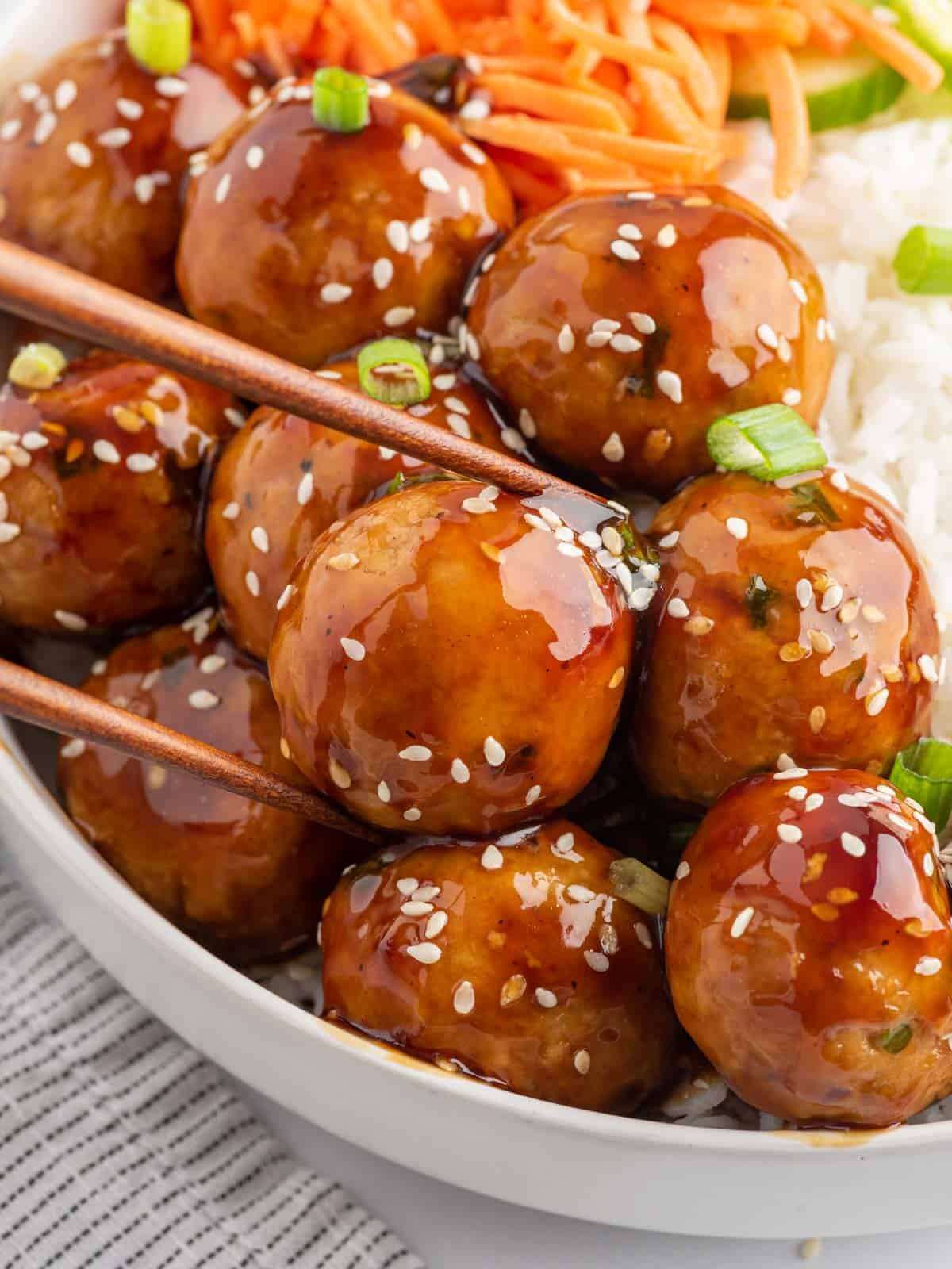 Chopsticks pick up a meatball coated in teriyaki sauce.