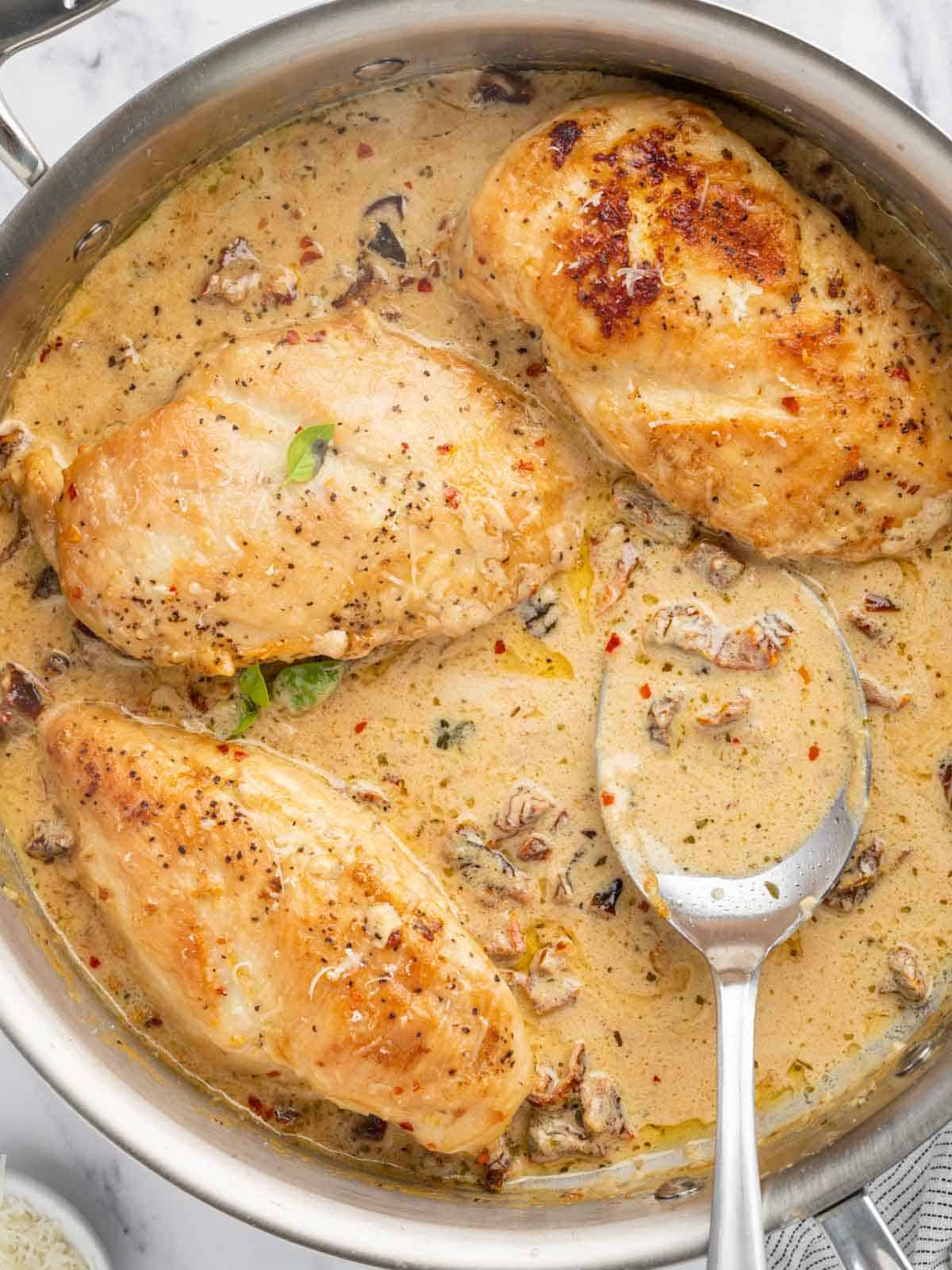 One skillet chicken and sundried tomatoes with a serving spoon.