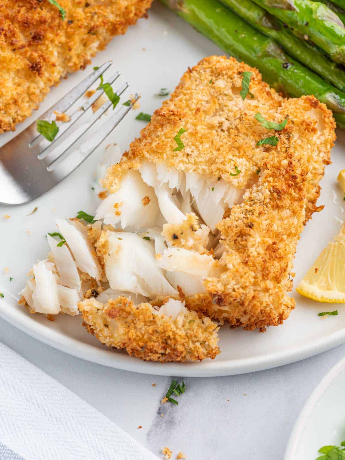 A fork flakes air fried cod on a plate.